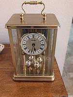 Front view of the brass and glass Verichron mantle clock showing clock face and rotating balls pendulum.