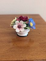 Angled side view of the vintage Denton China bone china figurine with multicolored flowers on a wood surface.