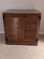 Front view of the vintage Ethan Allen record cabinet showing closed louvered doors with dark metal corner brackets and small round knobs.