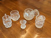 Photo of six Waterford crystal serving pieces arranged on wooden table: creamer, sugar dish with lid, toothpick holder, medium lidded dish, condiment jar with lid, and small lidded dish.
