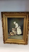 Full view of the vintage print featuring the lady in white bonnet by a wooden tub, in an ornate gilt frame.