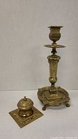 Brass candle holder and brass inkwell side by side showing overall condition and design.