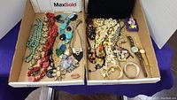 Wide view of two trays filled with assorted costume jewelry including necklaces, brooches, watches, and bracelets.