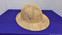 Side angle view of the woven safari style hat on a purple cloth background.