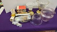 Full view of the lighting accessories lot showing two ceiling light fixtures with clear and mauve glass shades, assorted replacement bulbs, and boxed eight picture lamp.