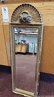 Front view of the gilt framed mirror showing decorative shell and scroll detail at top and rectangular reflective glass.