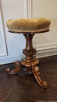 Full front view of round piano stool showing tufted cushion, carved wood pedestal and three scroll legs