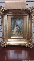 Front view showing ornate gold frame and romantic couple painting on swing surrounded by birds.