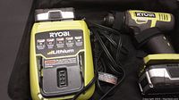 Ryobi cordless drill with attached battery inside carrying case, charger with cord beside it