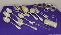 Overview of flatware, napkin rings and purse on purple background