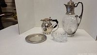 Full view of all items: embossed silver topped crystal wine decanter, silver plate jug with Bakelite handle, crystal swan, small silver plate dish.