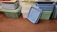 Photo showing stacks of large green and medium blue plastic storage bins with lids, along with two translucent clear bins.