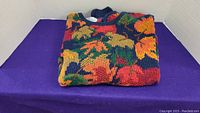 Folded colorful hand knitted sweater with autumn leaf pattern on navy background.