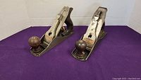 Front angle view of both bench planes on purple background showing the wood front knobs and cast iron bodies