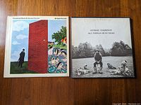Front covers of 'Wonderwall Music' and 'All Things Must Pass' vinyl albums by George Harrison on wooden surface.