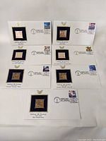 Seven white presentation cards with bronze replica stamps and commemorative postage stamps arranged in two rows.