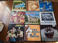 Nine vinyl record albums arranged on a wooden surface, showing covers with folk dancers from various European countries.