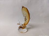 Side view of art glass dolphin figurine showing amber color and clear base with splash detail.