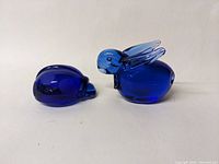 Side view of the cobalt blue glass ladybug figurine with rounded body and wing details, next to the bunny figurine with upright ears.