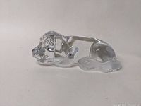 Side angle view of a clear glass puppy dog figurine lying down with visible ears, eyes, and front paws.