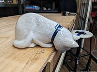 Side view of the cat figure showing crackle glaze and blue collar as it hangs over the edge of a table.