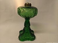 Front view of green glass oil lamp with bullseye pattern and ornate base showing metal burner top.