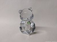 Front view of clear glass teddy bear figurine showing green heart detail on chest.