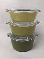 Stacked view of the three graduated round Pyrex Cinderella casserole dishes in Verde Green shades with their clear glass lids in place.