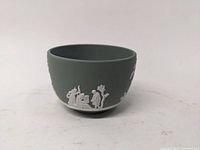 Photo of green Jasper Ware bowl showing classical figures in white relief on the side of the bowl.