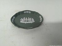 Top view showing the green oval Wedgwood Jasperware pin tray with white classical figures and floral decoration in center and around the rim.