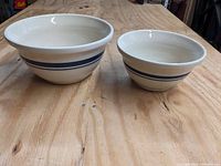 Two Roseville Friendship Pottery nesting bowls, larger 4-quart and smaller 2-quart, cream colored with blue bands sitting on a wooden surface.