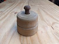 Side and top view of vintage wooden butter mold showing cylindrical shape, handle knob, and wood grain.