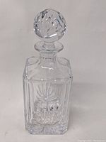 Front view of square crystal liquor decanter with detailed cuts and clear stopper on top.