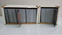 Two white cardboard boxes filled with a large number of Magic: The Gathering cards. Top cards held upright, showing edges of many sleeved or unsleeved cards.