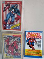 Front view of two Marvel Super Heroes trading card packs featuring Captain America and Spider-Man, next to a sealed Marvel Universe Series II Spider-Man trading card box with bonus holograms.