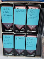 Front view showing eight Ultra PRO 100-count card protector boxes, each labeled with the card type and rarity (Black Rare Uncommon, Artifact, Red Rare Uncommon, Green Rare Uncommon)