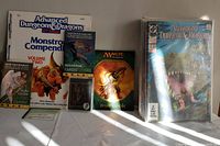 White table display showing Advanced Dungeons & Dragons Monstrous Compendium Volume Two, Classic Rules Book, Magic: The Gathering rulebook, and a stack of sleeved magazines.