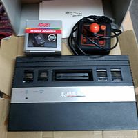 Atari 2600 console with Atari power adapter box, Slik Stik joystick, and manual inside a cardboard box.