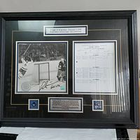 Full view of the framed commemorative display showing all elements including photo, score sheet and plaques.