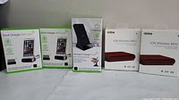 Lot showing 3 green and white boxed Dock Charger WiFi Cam units and 2 boxed iOttie iON Wireless Mini wireless chargers side by side on a table.