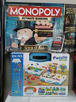 Monopoly Ultimate Banking game box showing front with Mr. Monopoly, bank cards, electronic banking unit and peg puzzle game box below
