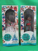 Front view of two dolls in original 'It's a Small World' packaging showing the dolls in traditional costumes and branded box design.