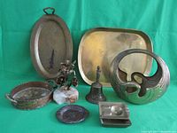 Photo showing a Korean swan brass basket, brass bell with figure handle, oval and rectangular platters, brass flower sculpture on stone base, and ashtrays.