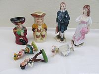 Seven porcelain figurines in a group shot, including Lefton China tall boy and girl, two Toby jugs, two small Portugal porcelain figurines, and a Dresden ballerina on a white background.
