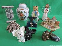 Overview of all items in lot on green background, showing a variety of figurines and souvenir pieces including ginger jar, wooden angel, and small sculptures.