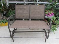 Front view of the garden glider bench showing woven fabric seat and backrest, metal frame, and armrests.