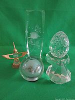 Overview of entire lot including crystal egg on base, etched pillar on rotating base, diamond paperweight, crystal and metal hummingbird, and painted crystal ball