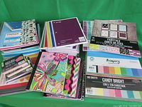 Photo showing an assortment of notebooks and various cardstock packs arranged on a table. Includes spiral-bound notebooks, decorative notepads, and multiple cardstock packs including fairytale, primary, candy bright, and marble.