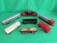 Seven Lionel train cars arranged on green background showing various engine and railcar types.