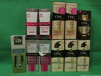 Full front view of all 11 boxed cosmetic products in line on green background showing brand names and product types.